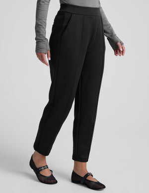 woman wearing a gray turtleneck and black tapered pants on a white background. 