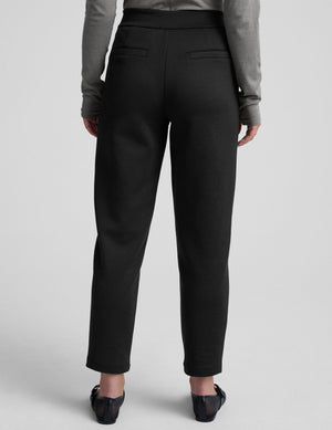 woman wearing a gray turtleneck and black tapered pants on a white background. 