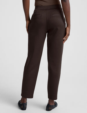 woman wearing brown tapered pants against a plain background. 