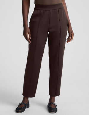 woman wearing brown tapered pants against a plain background. 