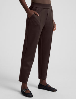 woman wearing brown tapered pants against a plain background. 