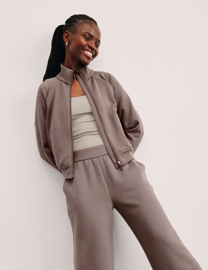 Woman wearing a brown zip-up jacket and pants on a plain background. 