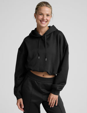 woman wearing a black cropped hoodie and pants on a plain background. 