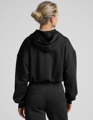 woman wearing a black cropped hoodie and pants on a plain background. 