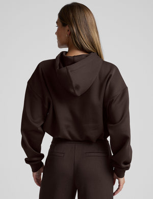 woman wearing a brown cropped hoodie and pants against a plain background. 