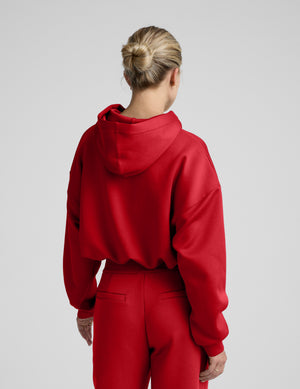 Woman wearing a red hoodie and pants on a plain background. 