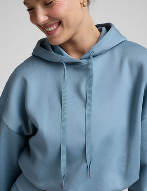 woman wearing a light blue hoodie and matching pants on a plain background. 