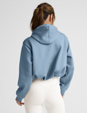 Woman wearing a light blue hoodie and white pants on a plain background. 