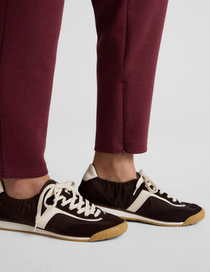 Burgundy SoftSpring Tapered Pant at ankle length with a small side zipper detail, styled with brown and cream sneakers.
