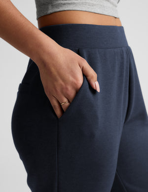 Woman wearing blue tapered ankle length pants against a plain background. 