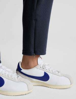 Woman wearing blue tapered ankle length pants against a plain background. 