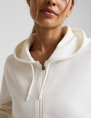 Woman wearing a white zip-up hoodie and black shorts against a plain background. 