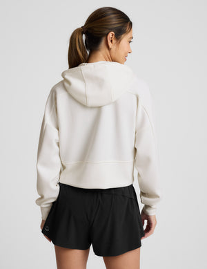 Woman wearing a white zip-up jacket and black shorts against a plain background. 