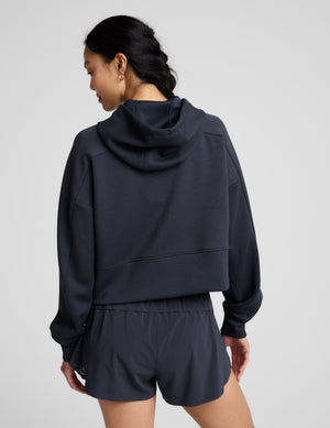 Woman is wearing a blue zip-up jacket and shorts against a plain background. 