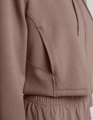 Woman wearing a brown full zip jacket and shorts against a plain background. 