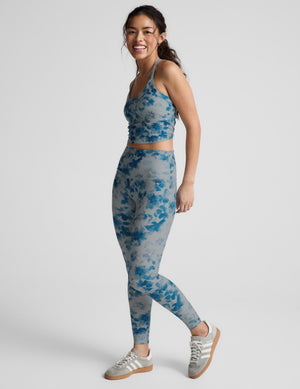 Woman wearing a blue floral sports bra and leggings on a light gray background. 