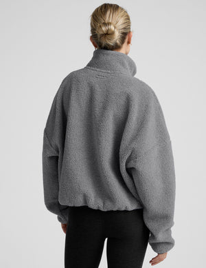 model wearing a gray fleece zip-up jacket against a plain background. 