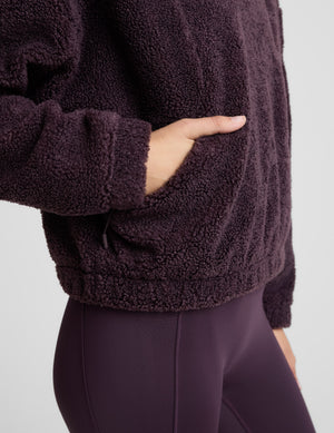 Woman wearing a purple quarter zip boucle jacket against a plain background. 