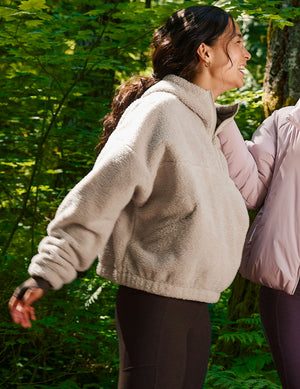 model wearing a beige fleece quarter zip hoodie in a forest setting. 