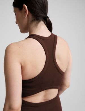 Woman wearing a brown dress with white sneakers on a light gray background.