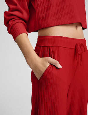 Person wearing red ribbed pants against a plain background. 