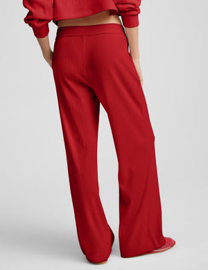 Person wearing red ribbed pants against a plain background. 