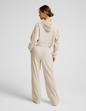 Woman wearing a beige hoodie and lounge pants on a plain background. 
