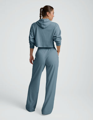 Person wearing a blue ribbed hoodie and pants on a white background. 