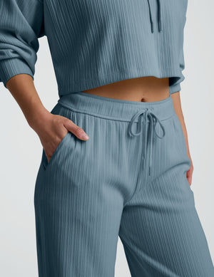 Person wearing a blue ribbed hoodie and pants on a white background. 