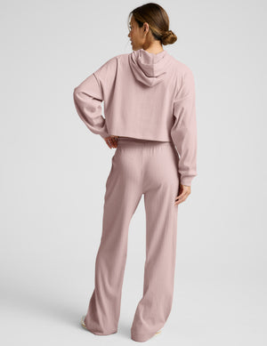 Woman wearing a pink ribbed cropped hoodie and pink ribbed pants on a light gray background. 