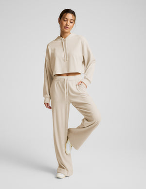 Woman wearing a beige cropped hoodie and pants on a light gray background. 