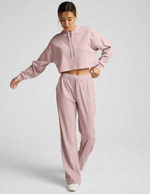 Woman wearing a ribbed cropped hoodie and pants on a plain background. 