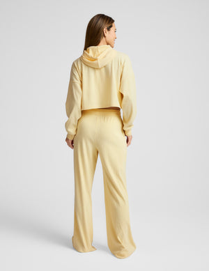 Woman wearing a yellow cropped hoodie and pants on a light gray background. 