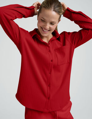 woman wearing a red ribbed button down shirt and red ribbed lounge pants against a plain background. 