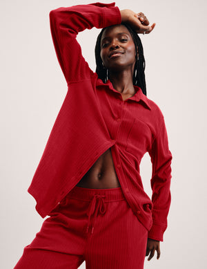 woman wearing a red ribbed button down shirt and red ribbed lounge pants against a plain background. 