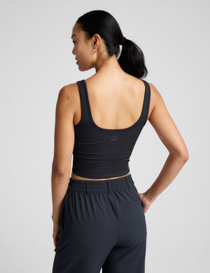 Woman wearing a blue ribbed cropped tank and blue pants against a plain background. 