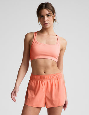 Woman wearing a coral sports bra and shorts set on a light gray background. 
