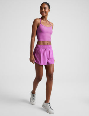 Woman wearing a purple cropped tank and purple shorts against a plain background. 