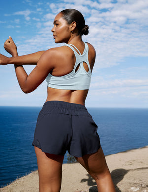Woman in athletic wear stretching by the ocean with a clear blue sky.