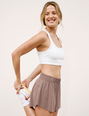 Woman wearing a white sports bra and brown shorts against a plain background. 