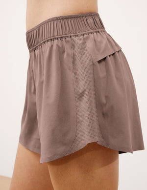 Woman wearing brown shorts against a plain background. 