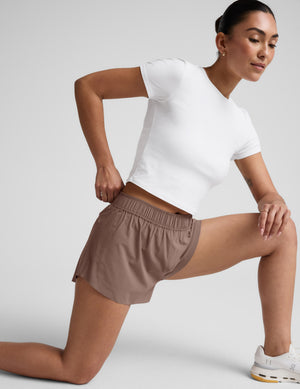 Woman wearing a white t-shirt and brown shorts against a plain background. 