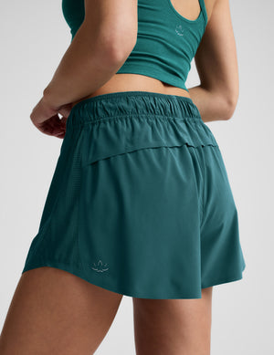 Woman wearing a green cropped tank and shorts against a plain background. 