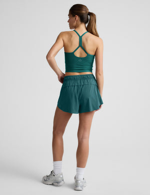 Woman wearing a green cropped tank and shorts against a plain background. 