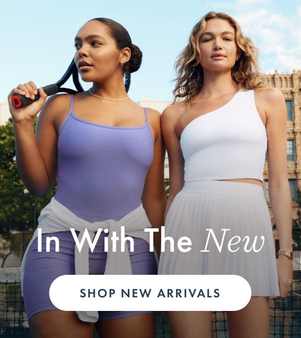 model on the left is wearing a blue slim strapped biker jumpsuit. model on the right is wearing a white one-shoulder cropped tank top and white pleated mini skirt. 