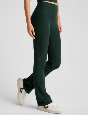 model wearing green high-waisted bootcut pants on a light gray background. 