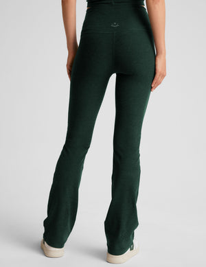 model wearing green high-waisted bootcut pants on a light gray background. 