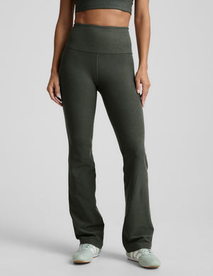 Person wearing green high-waisted bootcut pants on a light gray background. 