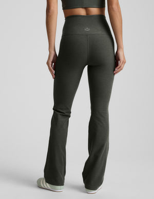 Person wearing dark green bootcut pants on a light gray background. 