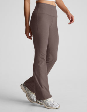 woman wearing brown high-waisted bootcut pants against a plain background. 